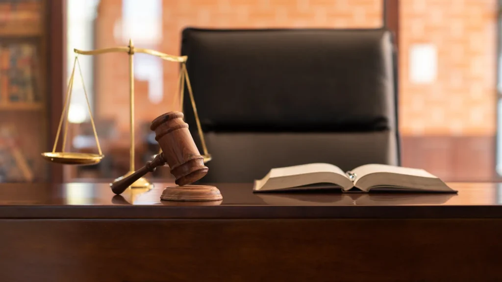 Wooden gavel and law book on a desk with a scale of justice in the background.