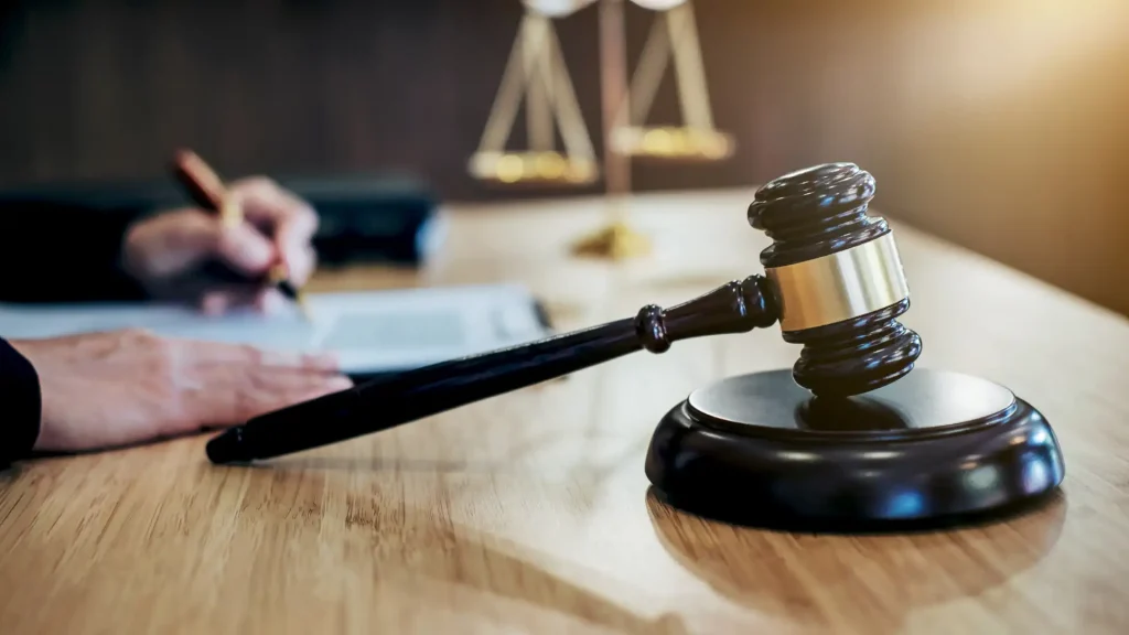 Close-up of a gavel with legal documents and scales of justice in the background."