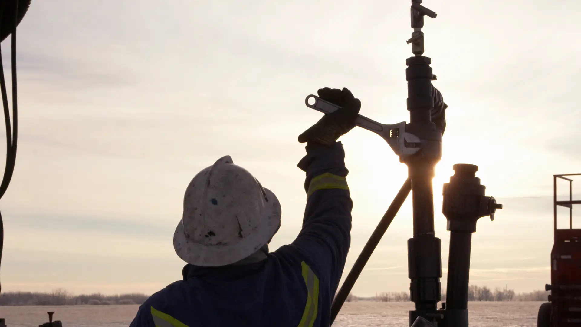 Worker using wrench on oil rig at sunrise