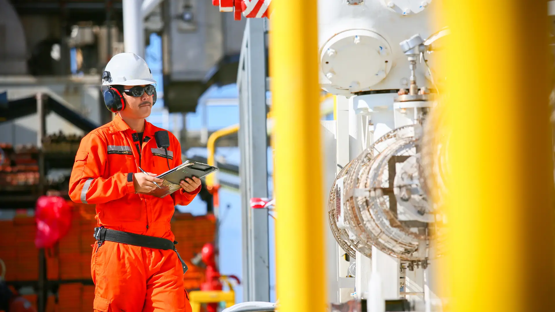 Worker in orange coveralls inspecting refinery equipment