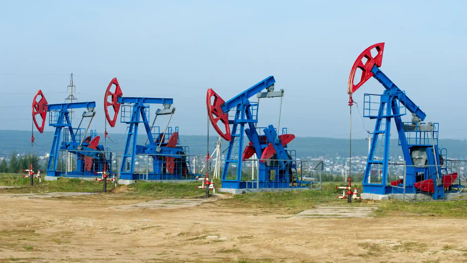 Blue and red pump jack oil rigs operating in a field with distant hills in the background.