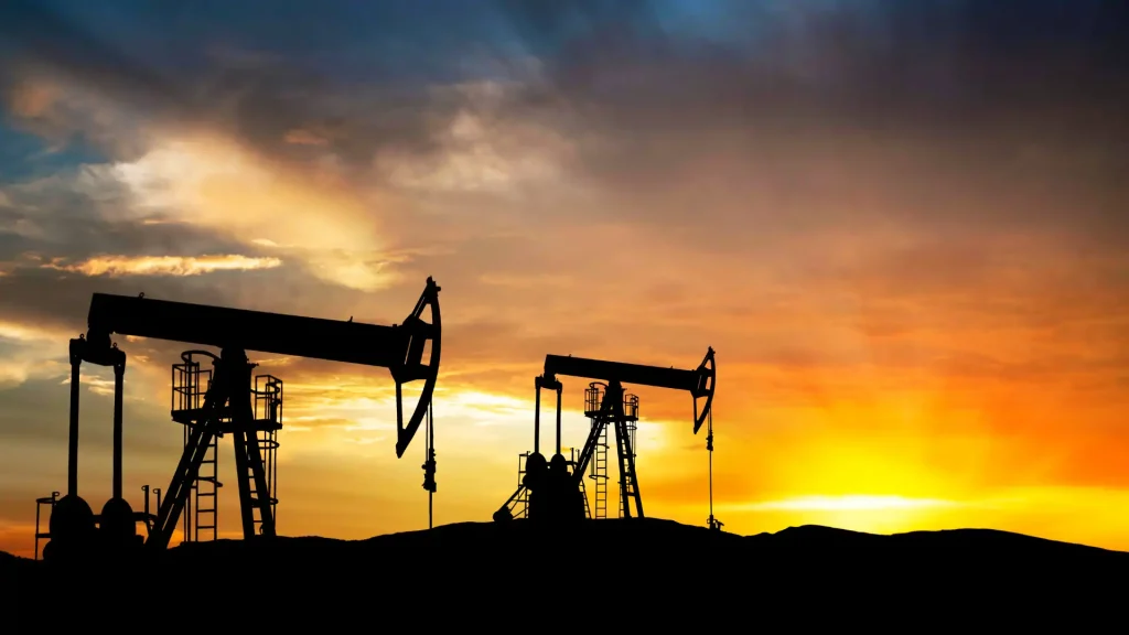 Oil pump jacks silhouetted against a dramatic sunset sky in an oil field.