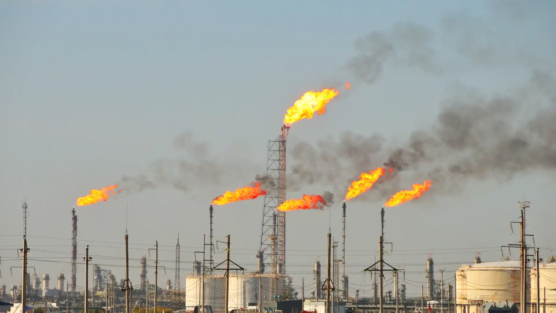 Gas flaring towers at an oil refinery releasing flames and smoke into the sky.