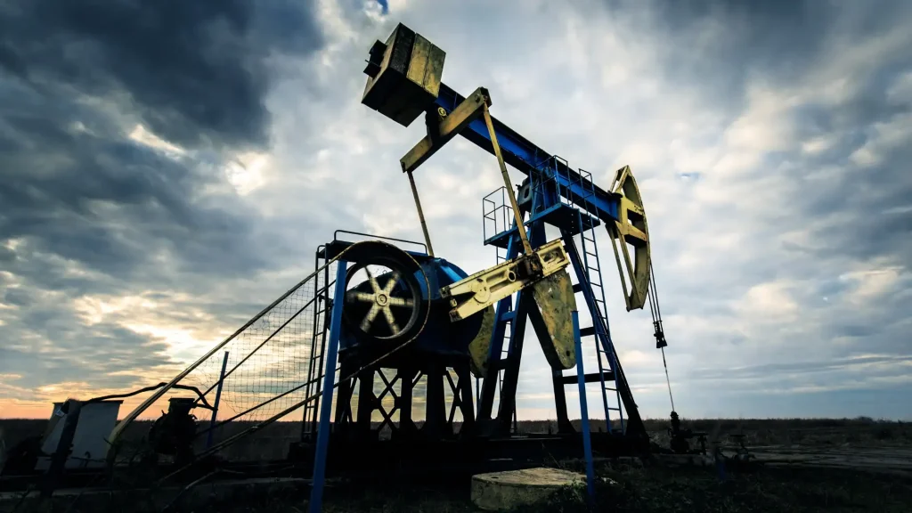 Oil pump jack operating in an open field under a cloudy sky.