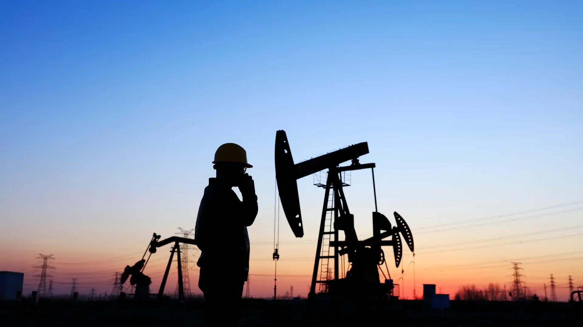 Silhouette of a worker in a hard hat and glasses, standing near oil pumps at sunset, symbolizing gas field worker safety and negligence liability.