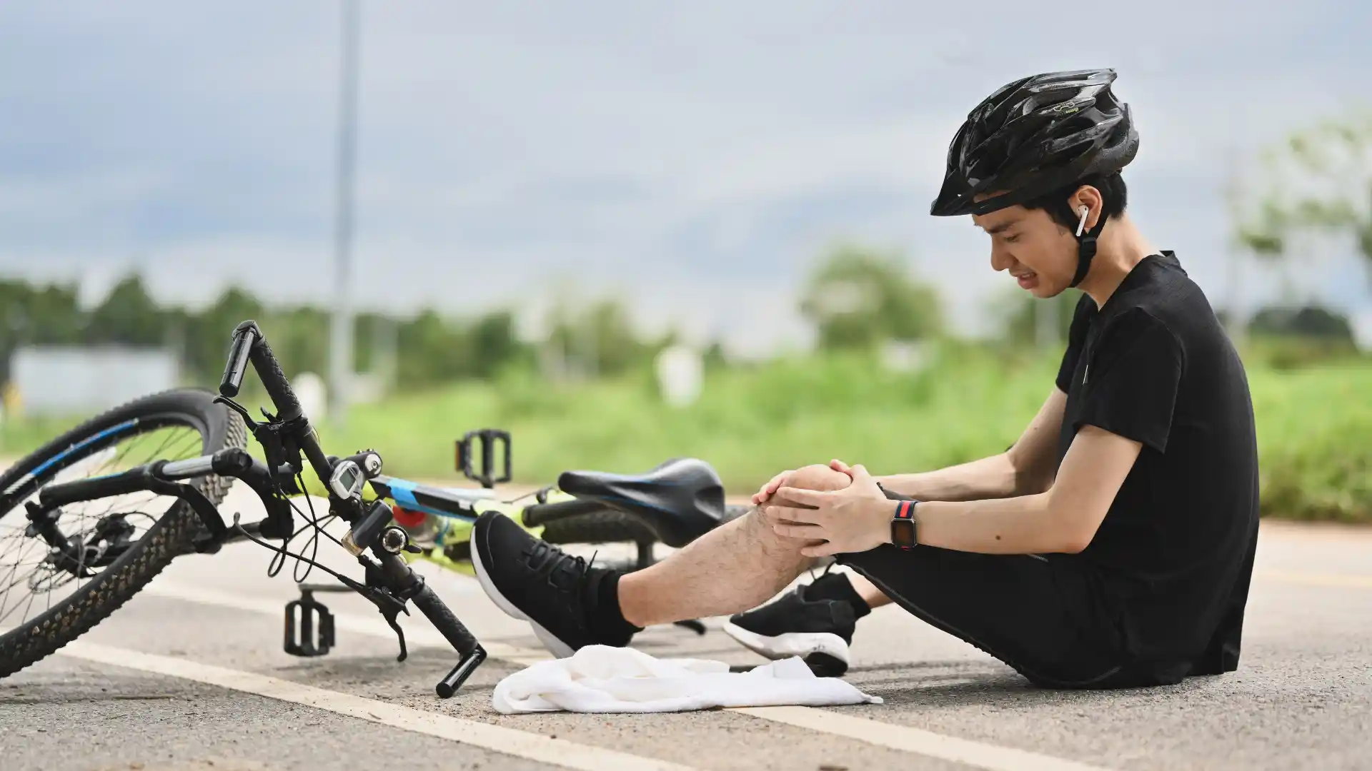 Injured cyclist sitting on the road holding his knee after a fall.
