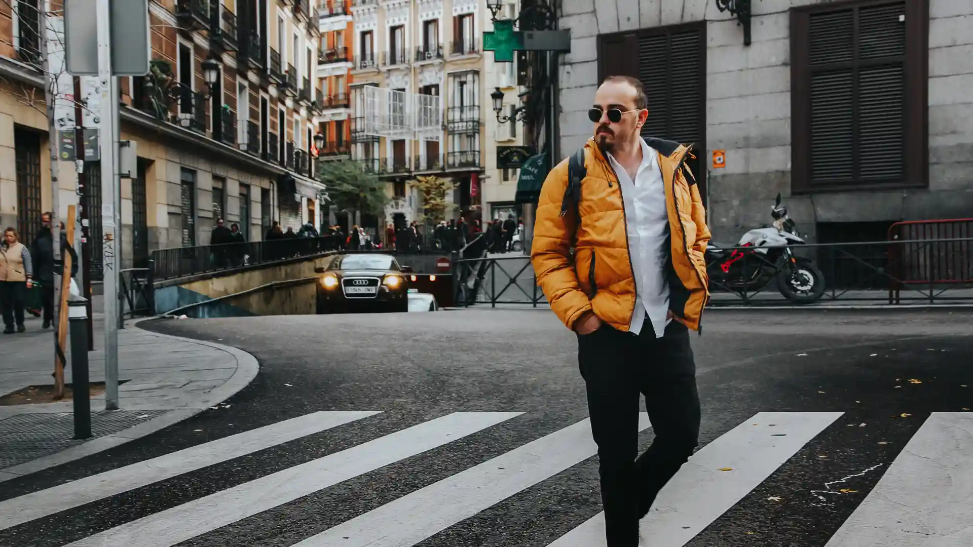 Man in a yellow jacket crossing a city street at a crosswalk.